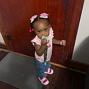 Ahla joined the competition — help win amazing prizes! toddler, child, pacifier, pink_bows, pink_shoes, jeans, pink_shirt, wooden_door, door_handle, floor_mat, indoor, standing, curly_hair, hair_beads, expression, flooring, home, person, cute, young_child