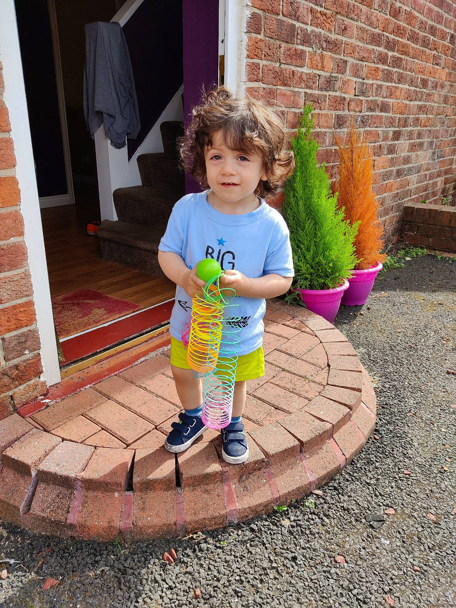 Lucas is registered to the contest to win money with this photo: asphalt, brick, brickwork, child, concrete, door, flooring, fun, grass, hairstyle, leisure, person, pink, plant, road_surface, shorts, sidewalk, standing, t_shirt, tints_and_shades