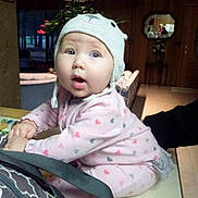 Kylie is registered to the contest to win money with this photo: architecture, baby, baseballcap, bonnet, building, cap, clothing, coat, face, furniture, hat, head, indoors, jacket, person, photography, plant, portrait, pottedplant, sitting