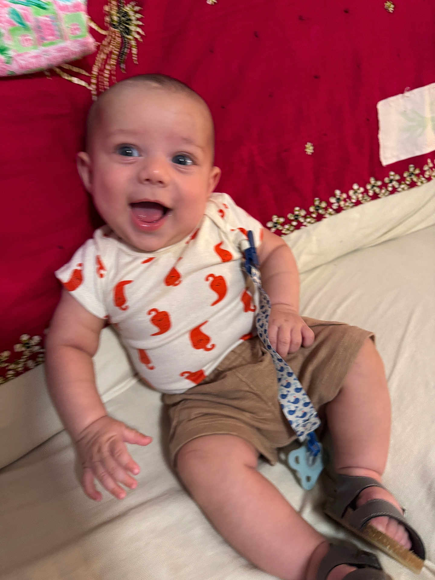 Franklin is registered to the contest to win money with this photo: baby, child, clothing, couch, fabric, face, footwear, hand, happy, indoor, infant, pacifier, pattern, person, red, shirt, shorts, skin, smile, white