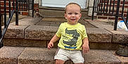 Carson is registered to the contest to win money with this photo: toddler, child, steps, stone, door, house_number, yellow_tshirt, shorts, sneakers, skateboard_graphic, railings, brick_wall, smiling, outdoor, front_door, person, young_child, casual_clothing, daylight, concrete