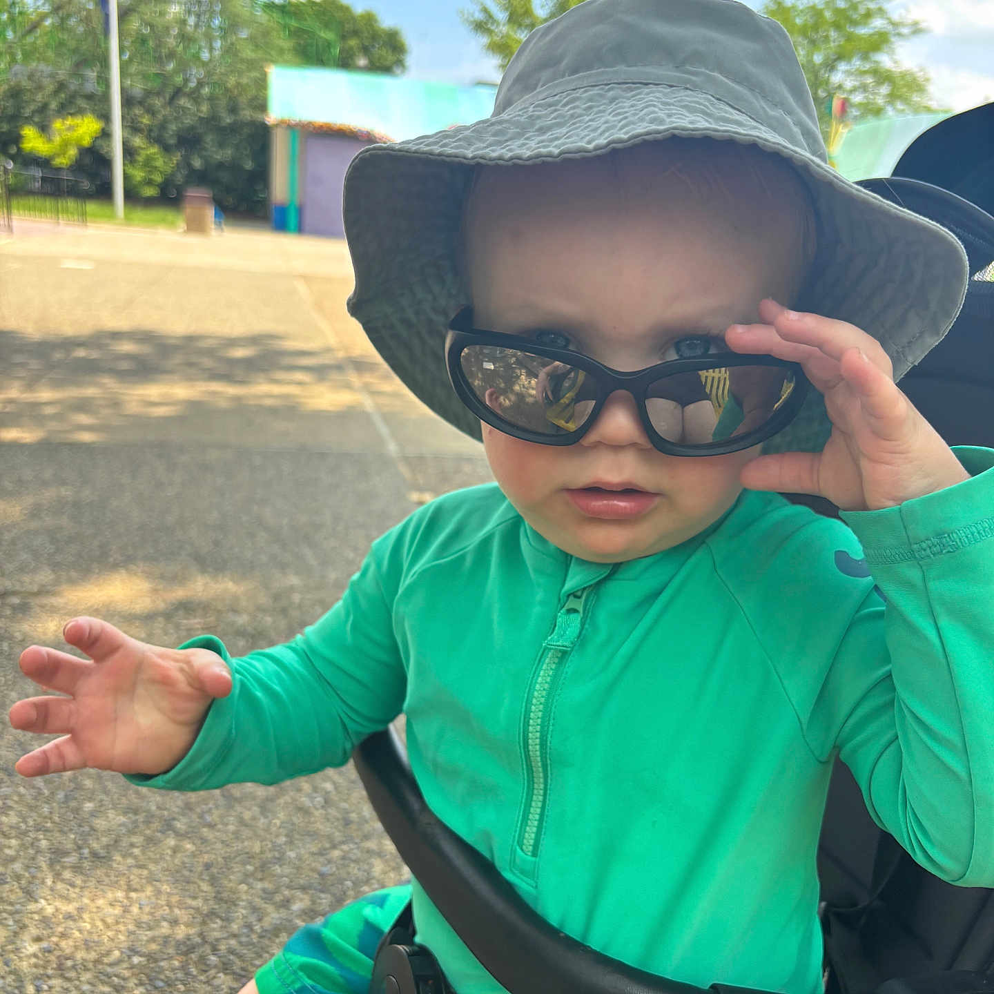 Carson joined the competition — help win amazing prizes! blue_sky, casual, child, cute, daytime, expression, face, green_clothing, hand, hat, outdoor, park, person, seatbelt, stroller, summer, sunglasses, sunny, toddler, trees