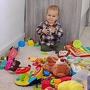 Timéo participe au concours pour gagner de l'argent avec cette photo : baby, carpet, child, clothing, colorful, cute, floor, happy, indoor, person, plastic_toys, play, playroom, plush, sitting, smiling, stuffed_animal, toddler, toys, wooden_panel