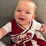 baby, smiling, cheerleader_outfit, maroon, cream, couch, gray, happy, infant, child, portrait, indoors, person, clothing, sitting, cute, cheer, short_hair, hand, face
