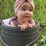 éliana a rejoint le concours — aidez-le/la à gagner de superbes lots ! baby, child, bucket, pink_turban, grass, wildflowers, outdoor, nature, greenery, cute, infant, portrait, curious, hands, face, headwear, summer, garden, playful, adorable
