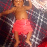 Jhcarri is registered to the contest to win money with this photo: baby, child, infant, plaid_blanket, red_shorts, lying_down, folded_clothes, person, indoor, skin, bare_chest, footwear_absent, hand, face, head, blanket, fabric, pattern, relaxing, casual