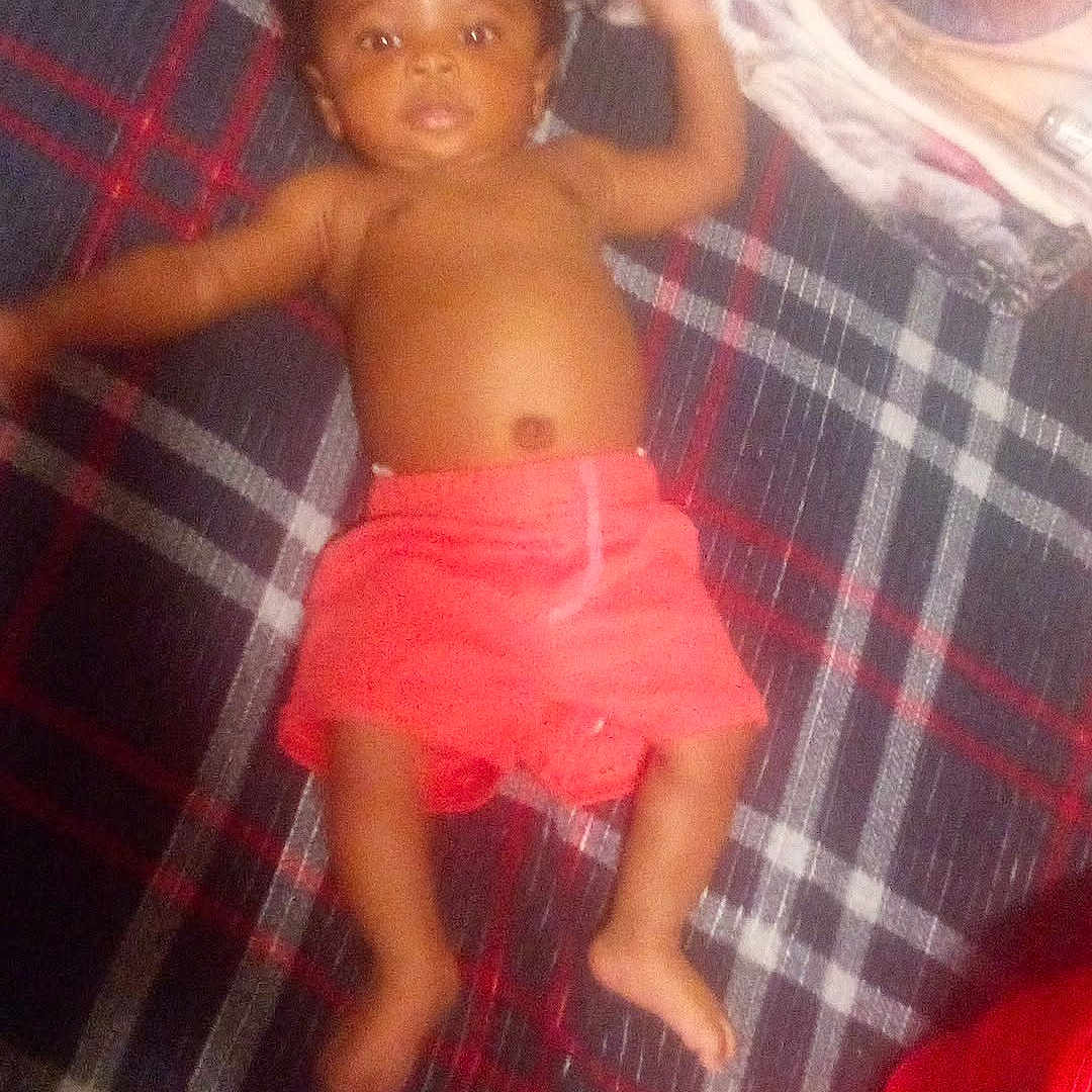 Jhcarri is registered to the contest to win money with this photo: baby, child, infant, plaid_blanket, red_shorts, lying_down, folded_clothes, person, indoor, skin, bare_chest, footwear_absent, hand, face, head, blanket, fabric, pattern, relaxing, casual