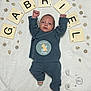 baby, infant, blue_clothing, blanket, wooden_letters, wooden_decorations, face, raised_arms, milestone_sticker, socks, lying_down, cute, newborn, soft_texture, celebration, name_letters, portrait, baby_gabriel, cozy, toddler