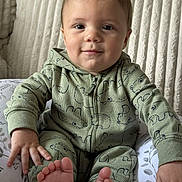 August is registered to the contest to win money with this photo: baby, child, comfort, cushion, cute, face, feet, green_clothing, hand, happy, home, hoodie, indoor, infant, patterned_clothing, portrait, sitting, smiling, soft_texture, young