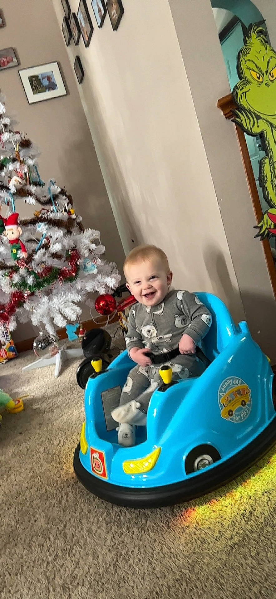 Daxton is registered to the contest to win money with this photo: automotive_design, baby, child, christmas_tree, event, fun, green, happy, head, joy, leisure, motor_vehicle, person, recreation, riding_toy, smile, tire, toddler, toy, tree