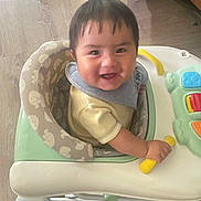 Erick is registered to the contest to win money with this photo: baby, walker, smiling, toy, indoor, floor, child, play, happy, face, clothing, bib, seat, hand, wood_floor, home, infant, cute, young_child, person
