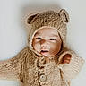 Erick is registered to the contest to win money with this photo: baby, infant, knitted_clothing, bear_ears, cute, portrait, child, warm, soft_texture, cozy, buttoned_sweater, hood, smiling, happy, indoor, closeup, face, small_hand, light_background, adorable