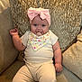 Taliah is registered to the contest to win money with this photo: baby, infant, pacifier, headband, bow, bib, couch, pillow, clothing, sitting, cute, indoors, child, smiling, portrait, comfortable, soft_furniture, happy, young_child, relaxed
