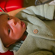 Thélio a rejoint le concours — aidez-le/la à gagner de superbes lots ! baby, bracelet, clothing, cozy, cute, face, hand, hat, holding, indoors, infant, knitwear, newborn, person, portrait, red_background, skin, sleepwear, small, tattoo