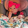 baby, infant, car_seat, pink_bow, blanket, floral_pattern, child, cute, face, headband, clothing, seatbelt, indoor, portrait, newborn, soft_texture, comfort, small_hands, expression, resting