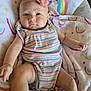 baby, infant, child, face, headband, flower, clothing, pastel_colors, rainbow, blanket, pattern, smiling_sun, cute, lying_down, soft_texture, indoors, person, skin, arm, leg
