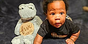 Kellan is registered to the contest to win money with this photo: baby, black_hair, blanket, child, cozy, crawling, curious, cute, five_months, frog, indoor, infant, lying_down, person, plush_toy, smiling, soft_toy, stuffed_animal, wooden_background, young_child
