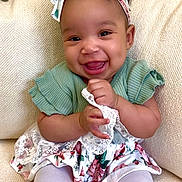 Kilyn is registered to the contest to win money with this photo: baby, child, smiling, headband, bow, green_top, floral_skirt, lace, sitting, couch, happy, cute, indoors, portrait, young_child, white_tights, furniture, person, infant, dressed_up