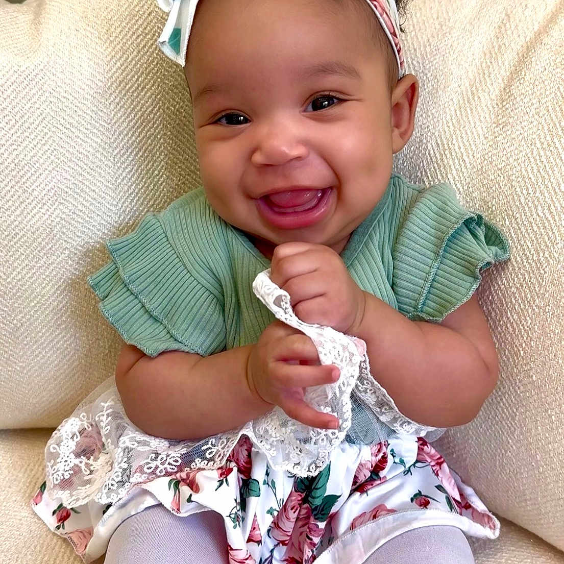 Kilyn is registered to the contest to win money with this photo: baby, child, smiling, headband, bow, green_top, floral_skirt, lace, sitting, couch, happy, cute, indoors, portrait, young_child, white_tights, furniture, person, infant, dressed_up