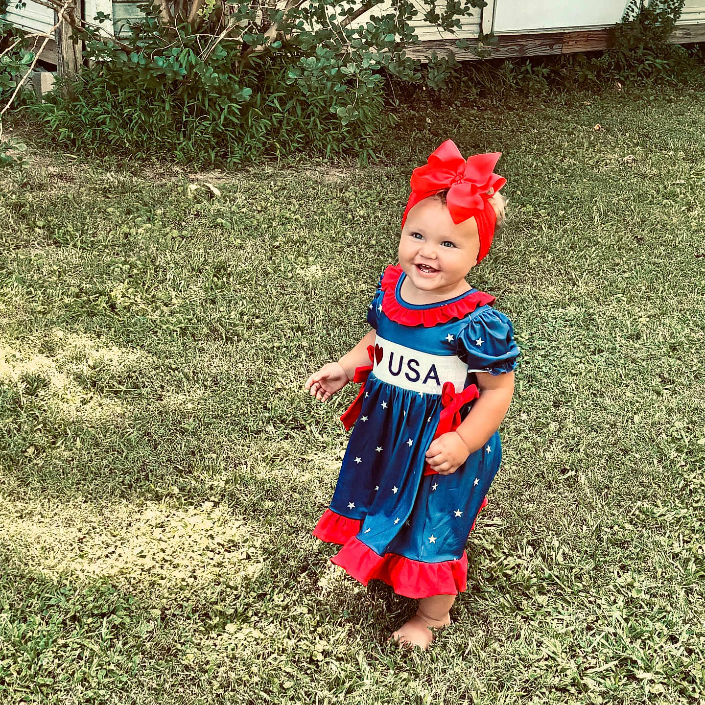 Kalayah joined the competition — help win amazing prizes! USA, barefoot, child, cute, dress, grass, greenery, happy, headband, house, outdoor, person, plants, red_bow, smiling, summer, toddler, walking, wood, young