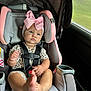 baby, child, car_seat, pink_bow, foot, seatbelt, car_interior, window, mesh_screen, clothing, infant, cute, serious_expression, sitting, safety_harness, headband, indoor, person, young_child, portrait