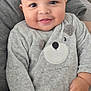 baby, smiling, onesie, grey_clothing, face, hands, cushion, patterned_background, indoor, closeup, child, cute, happy, infant, portrait, cozy, soft_texture, baby_clothes, person, seated