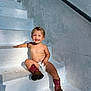 toddler, child, smiling, stairs, sunlight, outdoor, boots, diaper, bare_chest, happy, cute, playful, white, wall, shadow, curly_hair, young_child, sitting, person, daylight
