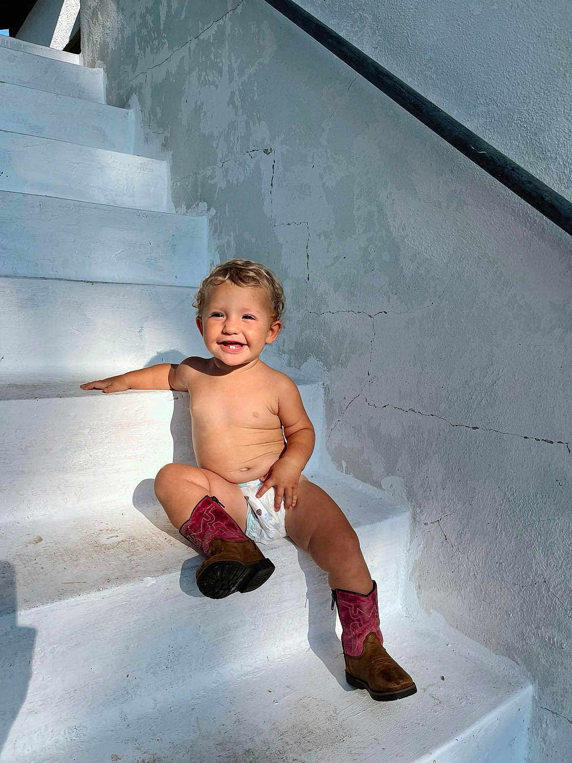 Cameron joined the competition — help win amazing prizes! toddler, child, smiling, stairs, sunlight, outdoor, boots, diaper, bare_chest, happy, cute, playful, white, wall, shadow, curly_hair, young_child, sitting, person, daylight
