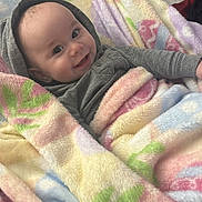 Ashton is registered to the contest to win money with this photo: baby, child, blanket, smile, hoodie, bed, cozy, infant, soft, happy, person, portrait, indoor, cute, warm, colorful, fabric, face, wrapped, comfort