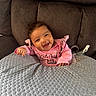 baby, smiling, pink_clothing, couch, gray_cushion, happy, infant, portrait, indoor, child, face, furniture, cozy, toddler, cute, relaxed, expression, comfort, young, seated