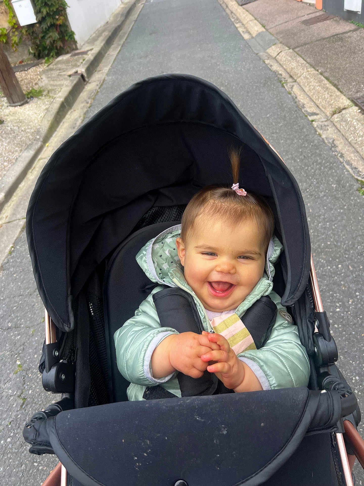 Lina participe au concours pour gagner de l'argent avec cette photo : baby, child, stroller, happy, smiling, outdoor, jacket, clapping, person, infant, pony_tail, road, sidewalk, black_stroller, cute, joyful, seated, winter_clothing, young_child, daytime