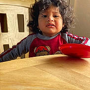 Liam joined the competition — help win amazing prizes! child, toddler, curly_hair, red_shirt, bear_design, wooden_table, wooden_chair, plate, indoor, furniture, person, expression, sitting, young_child, casual_clothing, face, portrait, daylight, home