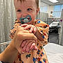 baby, child, pacifier, hand, hospital, bed, curtain, person, smiling, clothing, indoor, adult, holding, cute, infant, healthcare, happy, room, toy_pattern, portrait