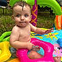 baby, child, inflatable_pool, pool_toy, pink_floatie, wet_hair, blue_eyes, outdoor, grass, summer, playtime, colorful, palm_tree_inflatable, water_droplets, cute, sitting, bare_chest, fun, nature, daytime