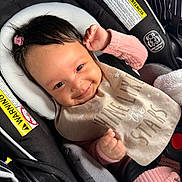 Camila is registered to the contest to win money with this photo: baby, car_seat, smiling, pink_clothing, bib, hair_clip, infant, child, safety_harness, cute, happy, indoors, person, seatbelt, warning_label, closeup, face, young_child, portrait, infant_clothing