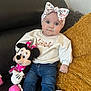 baby, child, blue_eyes, headband, floral, sweater, text_on_clothing, plush_toy, minnie_mouse, couch, cushion, blanket, jeans, sitting, indoor, cute, portrait, person, soft_lighting, comfort