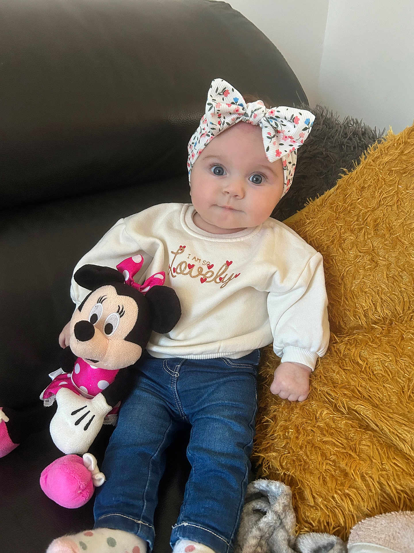 Victoire participe au concours pour gagner de l'argent avec cette photo : baby, child, blue_eyes, headband, floral, sweater, text_on_clothing, plush_toy, minnie_mouse, couch, cushion, blanket, jeans, sitting, indoor, cute, portrait, person, soft_lighting, comfort