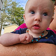 Tulsyn is registered to the contest to win money with this photo: arm, baby, blue_eyes, child, clothing, curious, face, freckles, hand, holding, house, necklace, outdoor, person, portrait, skin, sky, tattoo, trees, wide_eyes
