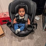 baby, child, infant, car_seat, sitting, wide_eyed, indoors, portrait, safety_harness, blue_pants, socks, cup_holder, floor, home, furniture, appliance, laundry, red_stool, photography, surprised