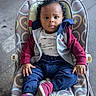 Zayne is registered to the contest to win money with this photo: baby, infant, child, portrait, sitting, bouncer, baby_seat, curly_hair, face, eyes, serious_expression, clothing, jacket, shirt, pants, sneakers, patterned_fabric, indoor, floor, photography