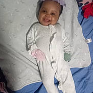 Layla is registered to the contest to win money with this photo: baby, smiling, onesie, mittens, blanket, bed, headband, infant, child, sleepwear, cute, lying_down, soft, comfort, happy, person, indoors, portrait, cozy, sleep