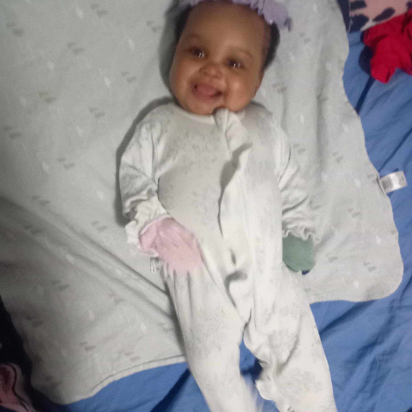 Layla is registered to the contest to win money with this photo: baby, smiling, onesie, mittens, blanket, bed, headband, infant, child, sleepwear, cute, lying_down, soft, comfort, happy, person, indoors, portrait, cozy, sleep