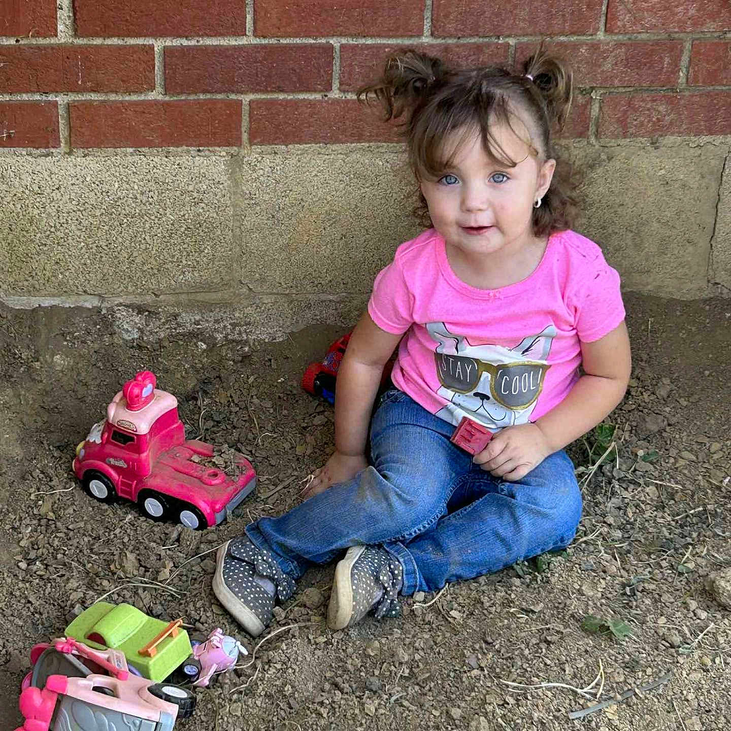 Hazelee is registered to the contest to win money with this photo: blue_eyes, brick_wall, casual_clothing, child, curious, cute, dirt, earrings, girl, jeans, outdoor, pigtails, pink_shirt, play, polka_dot_shoes, sitting, smile, toddler, toys, truck