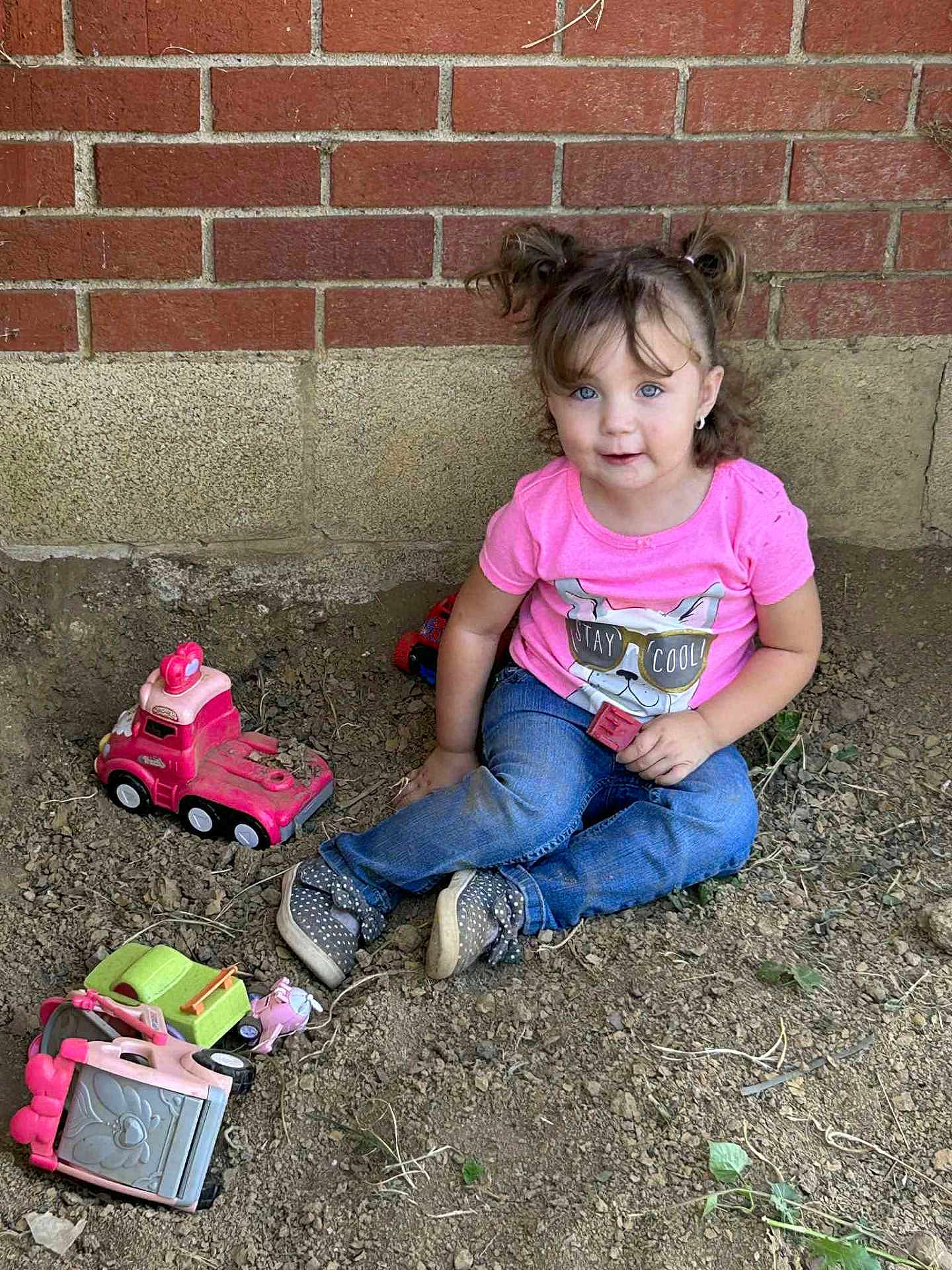 Hazelee is registered to the contest to win money with this photo: toddler, child, girl, toys, truck, pink_shirt, jeans, polka_dot_shoes, dirt, brick_wall, outdoor, play, pigtails, blue_eyes, sitting, casual_clothing, cute, smile, earrings, curious