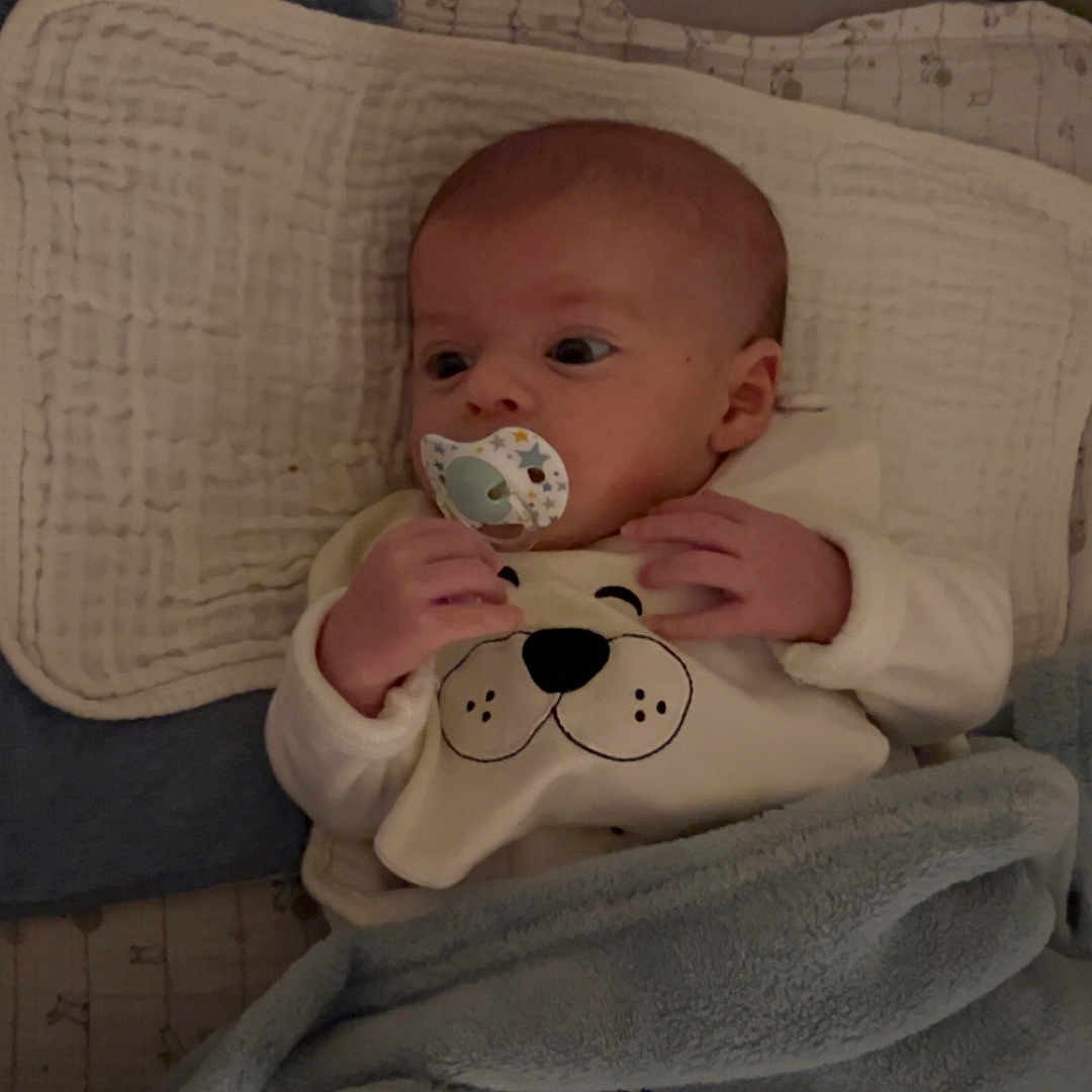 Daniel a rejoint le concours — aidez-le/la à gagner de superbes lots ! baby, bed, blanket, child, clothing, comfort, cozy, cute, expression, face, hand, indoors, infant, lying_down, pacifier, pillow, resting, sleepwear, soft, young