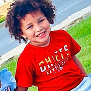 Joshua joined the competition — help win amazing prizes! child, smiling, curly_hair, red_shirt, outdoor, bench, grass, street, casual_clothing, happy, person, portrait, daylight, young, sitting, friends, playful, urban, toddler, cute