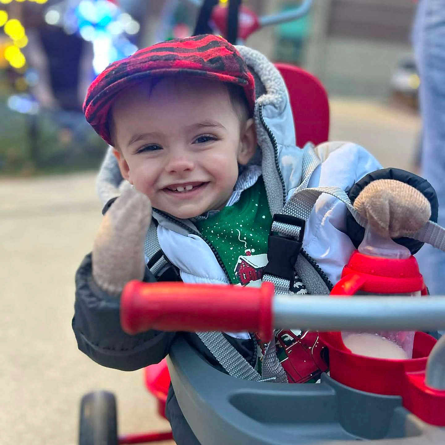Brody Dean is registered to the contest to win money with this photo: blurred_background, child, cozy, cute, face, green, happy, hat, holiday_lights, jacket, mittens, outdoor, portrait, red, smiling, stroller, toddler, toy, waving, winter_clothing