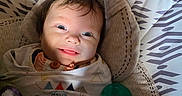 Anna is registered to the contest to win money with this photo: baby, smiling, infant, blanket, baby_seat, clothing, face, indoors, happy, child, pacifier, pattern, cozy, portrait, cute, young_child, expression, warm, soft_lighting, resting