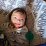 baby, smiling, infant, blanket, baby_seat, clothing, face, indoors, happy, child, pacifier, pattern, cozy, portrait, cute, young_child, expression, warm, soft_lighting, resting