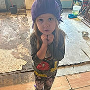 Willow is registered to the contest to win money with this photo: child, girl, purple_wig, mickey_mouse, shirt, leggings, socks, indoor, floor, cracked_floor, worn_floor, person, toy, window, door, bucket, shelf, food_cans, water_dispenser, expression